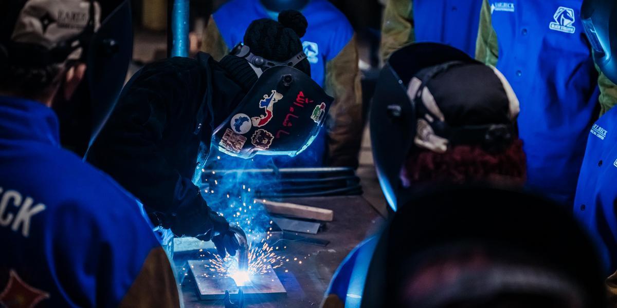 Instructor Jannah Madyun demonstrates welding to a class of students.
