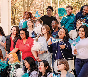 A group of students outside smiling, cheering, and holding AACC spirit items.