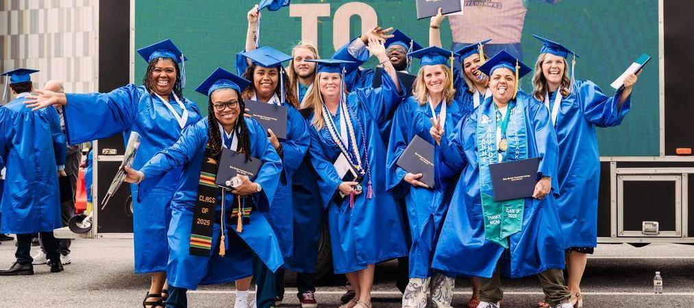 Group of students in graduation regalia posing for photo with AACC graphic on a truck in the background.