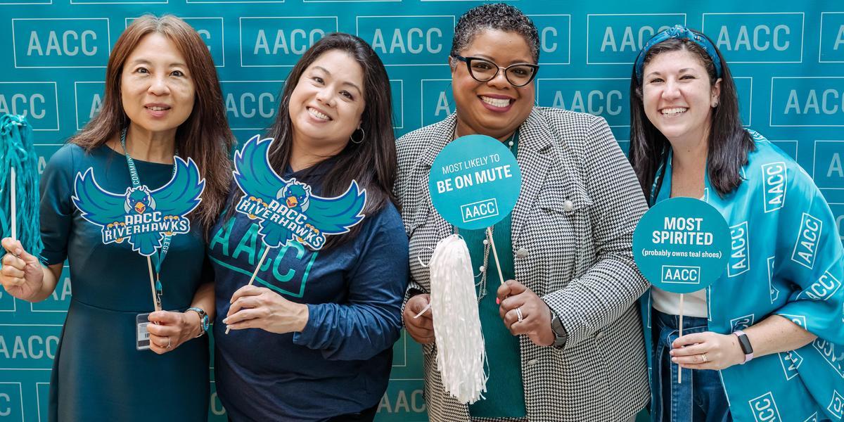 Four AACC staff members posing with AACC signs.