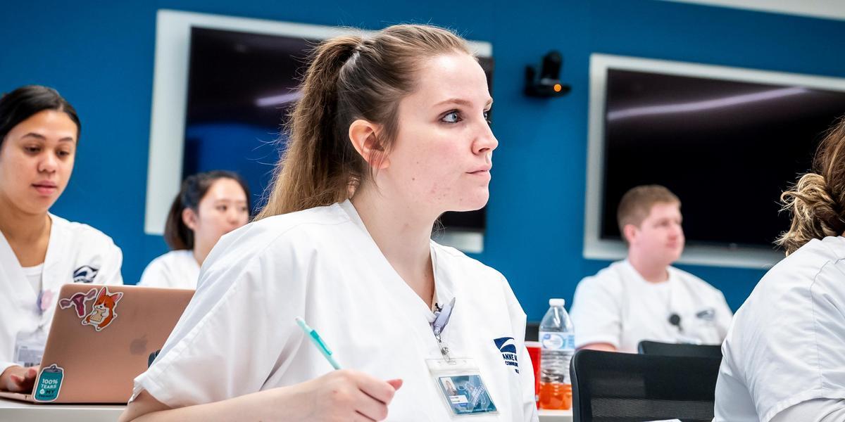 A nursing student wearing scrubs sitting in a classroom.