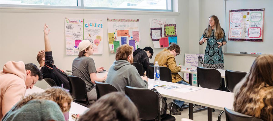 A teacher standing before a classroom of students. Bright papers hand on the wall.