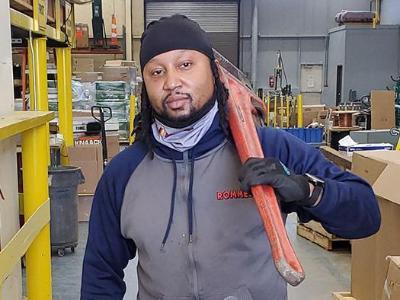 Teddy Strong standing in a warehouse with a piece of equipment over his shoulder.